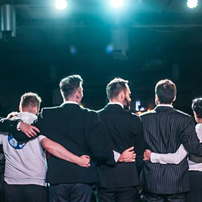 Actors bow to audience on stage after performance. Loud applause from crowd. Theatre scene. Obeisance to public. Back view